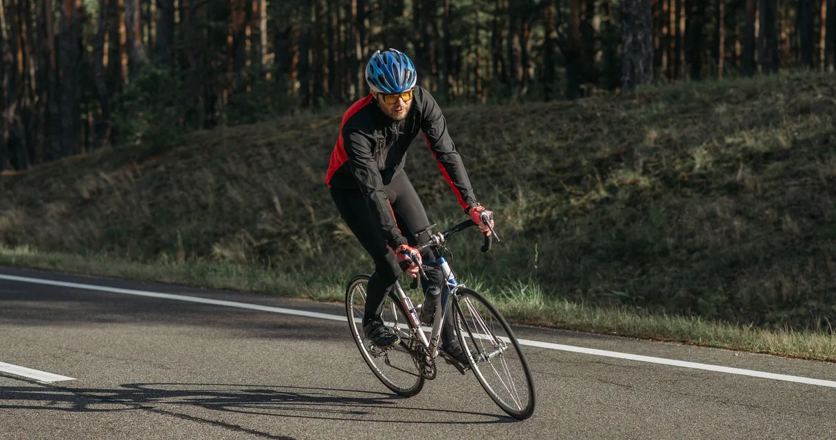 Ciclista de capacete azul pedalando em uma estrada asfaltada entre árvores
